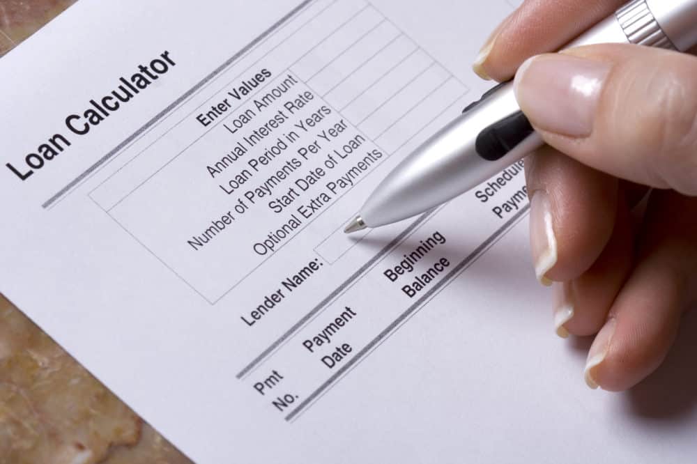 Close-up of a hand holding a pen above a printed loan calculator form, tailored for assisted living facility financing, with fields for loan details and lender name.