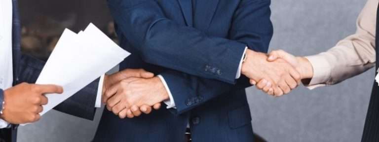 Three people in business attire shake hands confidently, with one person in the foreground holding papers related to an OIG Corporate Integrity Agreement.