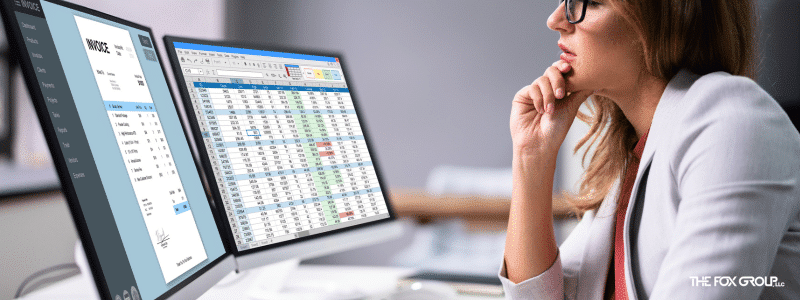 Person analyzing spreadsheets on dual monitors at a desk, hand on chin, wearing glasses and a focused expression, working diligently to increase medical practice collections.