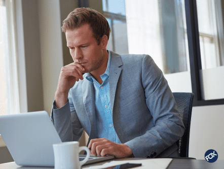 Man in suit sitting at desk in front of computer concentrating very hard. Represents the thought put into due diligence reviews in healthcare.